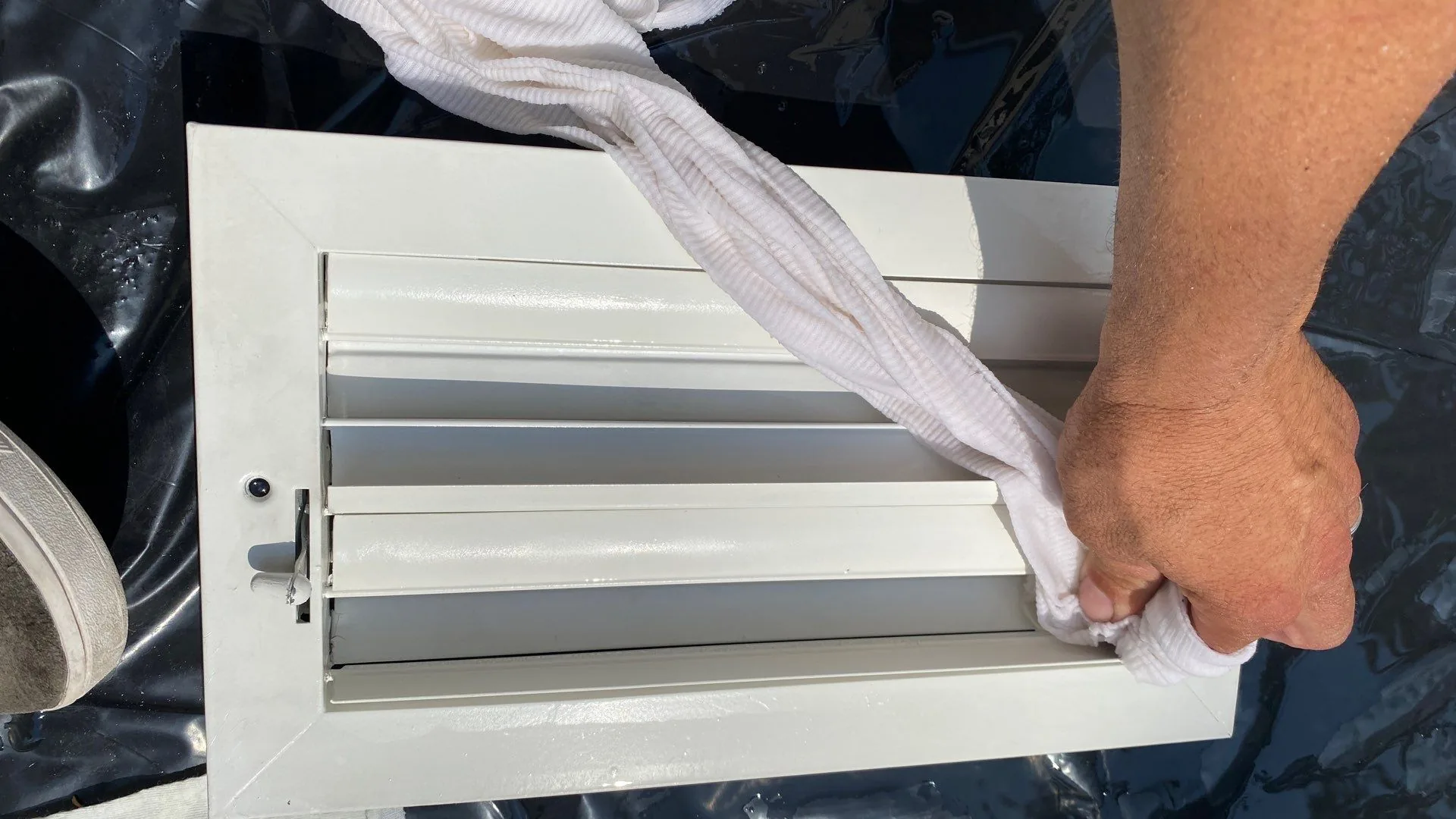Hand using a white cloth to wipe a removed white metal air register.